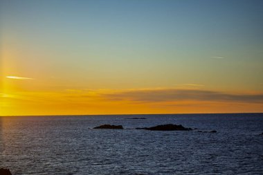 Küçük kayalık adalar ve derin mavi su üzerinde canlı altın ufuk ile minimalist okyanus gün batımı