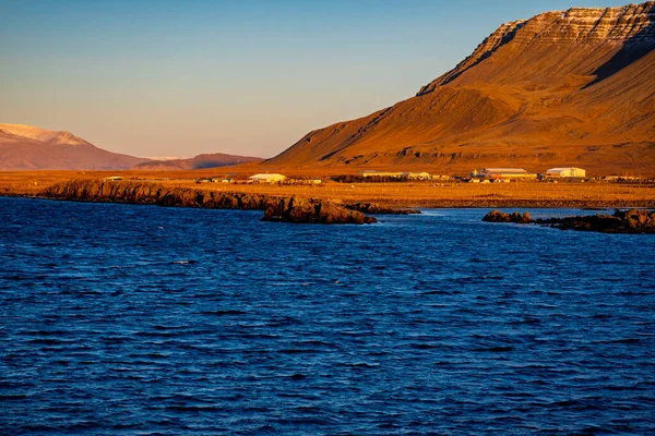 İzlanda 'daki Derin Mavi Deniz kıyısındaki Rocky Sahili ve Karlı Dağların Görkemli Altın Saati manzarası
