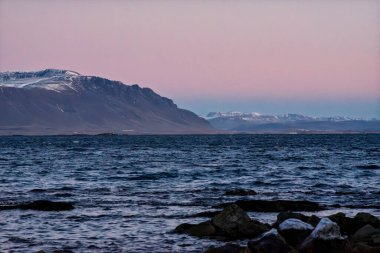 Pembe günbatımında İzlanda, Akranes 'te karlı dağların ve Atlantik Okyanusu kıyısının panoramik manzarası