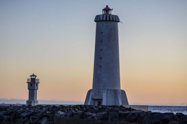 İzlanda 'daki Akranes' in tarihi ve yeni beyaz deniz fenerleri gün batımında kayalık sahilde duruyor.
