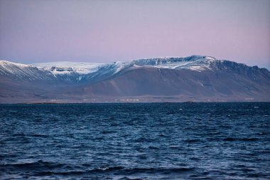 Akranes İzlanda 'daki Derin Mavi Deniz' in karşısındaki görkemli kar örtülü dağlar Alacakaranlık 'ta