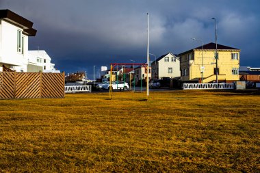 İzlanda 'da sakin bir yerleşim yeri. Gün batımında dramatik karanlık fırtına bulutları altında boş oyun alanı salınımları var.