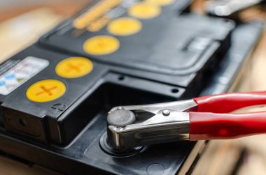 12 V 'lik otomotiv kurşun asit pili şarj ediliyor. Bir kırmızı metal timsah kıskacı, sarı kapaklı siyah pil kaplamasının pozitif uçlarına bağlıdır..