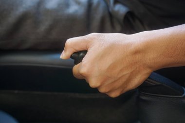 Close-up of a man holding the handbrake while sitting in a car.