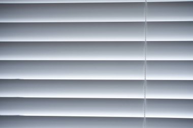 Beyaz Venedik panjurlarının yakın çekim görüntüsü, yatay çizgiler ve gölgeler oluşturarak modern iç mekanlarda gizlilik ve ışık kontrolü sağlar..