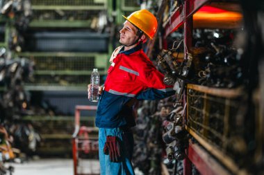 Güvenlik teçhizatındaki bir erkek teknisyen uzun bir fiziksel çalışma gününden sonra yorgunluk ve kas ağrısı belirtileri gösteriyor. Endüstriyel ve mekanik çalışma ortamlarının zorlu doğasını vurguluyor..