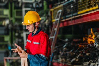 Güvenlik teçhizatındaki bir erkek teknisyen uzun bir fiziksel çalışma gününden sonra yorgunluk ve kas ağrısı belirtileri gösteriyor. Endüstriyel ve mekanik çalışma ortamlarının zorlu doğasını vurguluyor..