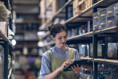 Aile şirketinde çalışan bir kız, iyi organize edilmiş bir depoda bulunan el bilgisayarlı bir tarayıcıyla perakende ve toptan satış işlemleri için verimli hisse senedi kontrolü yaptığını doğruladı.