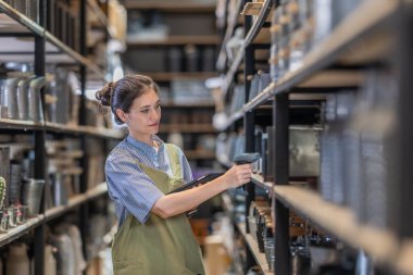 Aile şirketinde çalışan bir kız, iyi organize edilmiş bir depoda bulunan el bilgisayarlı bir tarayıcıyla perakende ve toptan satış işlemleri için verimli hisse senedi kontrolü yaptığını doğruladı.