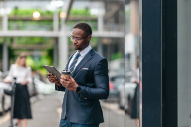 İki iş arkadaşı elektrikli bir scooterla şehir boyunca gidip geliyor, parlak cam binalar arasında ofise doğru gidiyor ve modern, çevre dostu bir iş kültürü sergiliyor..