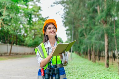 Dişi çevre araştırmacısı orman koşullarını dürbün kullanarak gözlemliyor, not alıyor, veri iletiyor. Çevresel izleme, biyolojik çeşitlilik takibi, kadınların dosyalanmış orman değerlendirmelerindeki rolü.