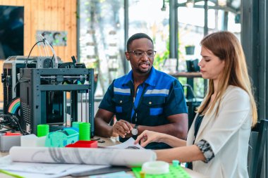 Erkek mühendis kadın ürün tasarımcısıyla işbirliği yapar, tasarım stüdyosunun teknik planlarını gözden geçirir. 3D baskı ve ürün geliştirmede disiplinler arası takım çalışması, planlama, çizimler vurgulanıyor