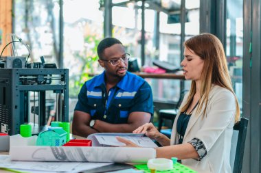 Erkek mühendis kadın ürün tasarımcısıyla işbirliği yapar, tasarım stüdyosunun teknik planlarını gözden geçirir. 3D baskı ve ürün geliştirmede disiplinler arası takım çalışması, planlama, çizimler vurgulanıyor