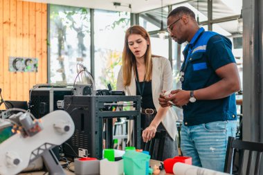 Erkek mühendis kadın ürün tasarımcısıyla işbirliği yapar, tasarım stüdyosunun teknik planlarını gözden geçirir. 3D baskı ve ürün geliştirmede disiplinler arası takım çalışması, planlama, çizimler vurgulanıyor