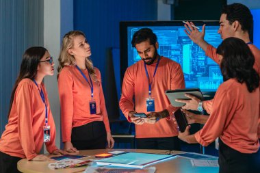 Eşleşen turuncu tişörtlü ürün ekibi masa etrafında işbirliği yapar, kablolar, renk örnekleri, analitik panelli mobil uygulama prototipleri gözden geçirir. UX UI sürat planlama oturumu yakalanıyor