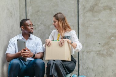 Kadın çalışan bir kutu ofis eşyası taşırken, Afrikalı erkek çalışan onu dışarıda cesaretlendiriyor. Ekonomik kriz ve işyeri desteği ve dayanıklılığı sırasında iş kaybının yansıtılması