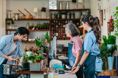 Aile seramik mağazasında, bir anne-kız tezgahtaki erkek müşteriye dostane bir hizmet sunarak, sıcak perakende konukseverliği ve ev eşyaları alışverişini ön plana çıkarıyor..