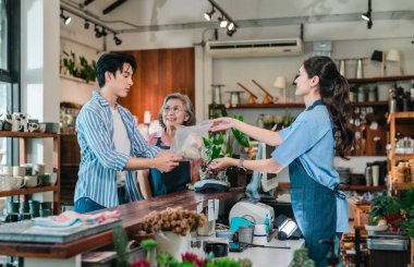 Aile seramik mağazasında, bir anne-kız tezgahtaki erkek müşteriye dostane bir hizmet sunarak, sıcak perakende konukseverliği ve ev eşyaları alışverişini ön plana çıkarıyor..