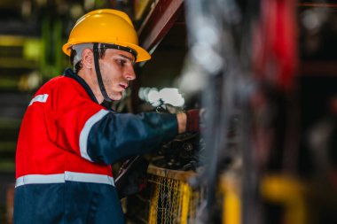 Erkek teknisyen, depo raflarındaki otomotiv parçalarının envanterini incelemek ve kontrol etmek için barkod tarayıcısı ve dijital tablet kullanır.