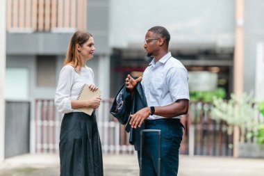 İki profesyonel modern şehir şeridinde yürüyor ve konuşuyor. Şirket seyahatleri, iş seyahatleri ve çevik iş hareketliliğinin sinyallerini veren bir bavul çekiyorlar..