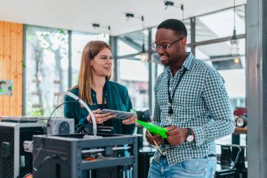 İki ürün tasarımcısı tasarım stüdyosunda 3 boyutlu prototipleri inceleyip tartışıyor. Ürün geliştirmede katkı sağlayan üretim teknolojisi kullanılarak takım çalışmasını, yaratıcılığı ve uygulamalı testleri vurgulamak