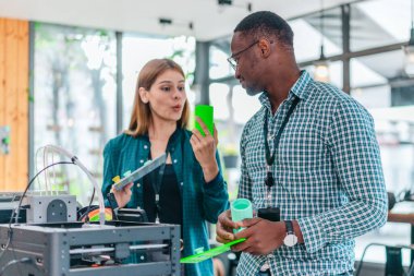 İki ürün tasarımcısı tasarım stüdyosunda 3 boyutlu prototipleri inceleyip tartışıyor. Ürün geliştirmede katkı sağlayan üretim teknolojisi kullanılarak takım çalışmasını, yaratıcılığı ve uygulamalı testleri vurgulamak