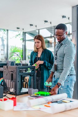 İki ürün tasarımcısı tasarım stüdyosunda 3 boyutlu prototipleri inceleyip tartışıyor. Ürün geliştirmede katkı sağlayan üretim teknolojisi kullanılarak takım çalışmasını, yaratıcılığı ve uygulamalı testleri vurgulamak