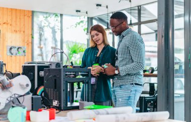 İki ürün tasarımcısı tasarım stüdyosunda 3 boyutlu prototipleri inceleyip tartışıyor. Ürün geliştirmede katkı sağlayan üretim teknolojisi kullanılarak takım çalışmasını, yaratıcılığı ve uygulamalı testleri vurgulamak