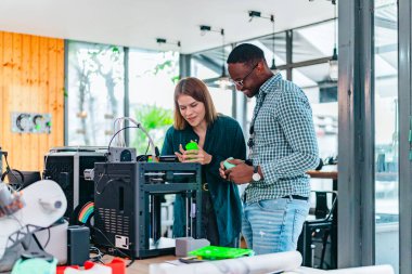 İki ürün tasarımcısı tasarım stüdyosunda 3 boyutlu prototipleri inceleyip tartışıyor. Ürün geliştirmede katkı sağlayan üretim teknolojisi kullanılarak takım çalışmasını, yaratıcılığı ve uygulamalı testleri vurgulamak