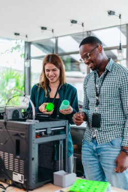 İki ürün tasarımcısı tasarım stüdyosunda 3 boyutlu prototipleri inceleyip tartışıyor. Ürün geliştirmede katkı sağlayan üretim teknolojisi kullanılarak takım çalışmasını, yaratıcılığı ve uygulamalı testleri vurgulamak