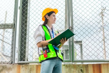 Kadın bir saha analisti pompa istasyonunda inceleme ve veri toplama yapar. Kamu hizmetleri altyapı yönetiminde teknik alan çalışması, kalite kontrolü ve karbon ayak izi denetimi.