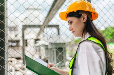 Kadın bir saha analisti pompa istasyonunda inceleme ve veri toplama yapar. Kamu hizmetleri altyapı yönetiminde teknik alan çalışması, kalite kontrolü ve karbon ayak izi denetimi.