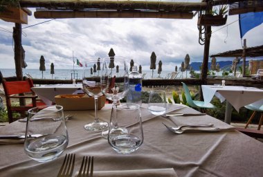 Denizden birkaç metre uzakta, Ligurian Rivierası 'ndaki bir kasabada, kumdaki bir restoranda masaları.