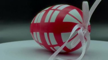 Kırmızı-beyaz Paskalya yumurtasının 4K videosu. Pembe kurdeleli, açık ve koyu arkaplanlı.