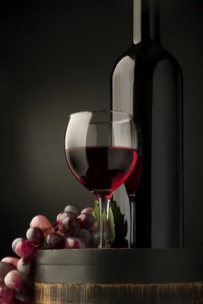 Vidrio con vino tinto, botella, vid y viejo, barril de madera aislado en gradiente negro — Foto de Stock