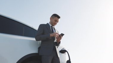 Beyaz adam akıllı telefon kullanıyor ve elektrikli araçlarla bağlantı kuruyor. Arabadaki aküyü şarj etmek için. Elektrikli arabayı şarj eden fiş.
