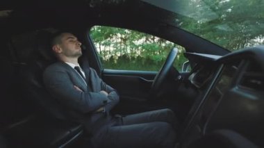 Otonom otomatik pilotsuz elektrikli arabada otomatik direksiyon başında uyuyan bir iş adamı. Lüks elektrikli bir araçla kırsal yolda derin uykuya dalmış bir adam..