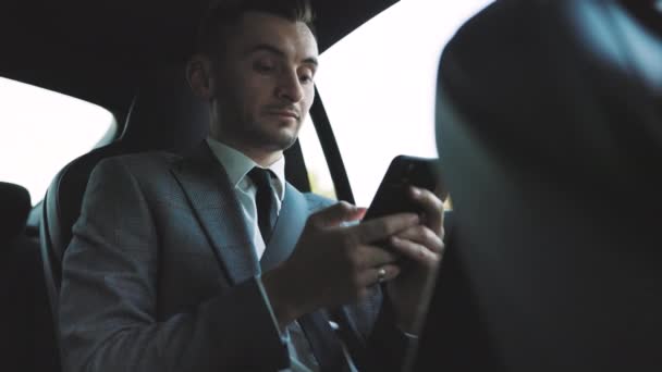 Atrakcyjny młody biznesmen korzystający z telefonu komórkowego do zdalnej komunikacji podczas odpoczynku w samochodzie. Ludzie i media społecznościowe. Mężczyzna profesjonalista korzystający z telefonu w automobilu. Mężczyzna smsy na smartfonie. — Wideo stockowe