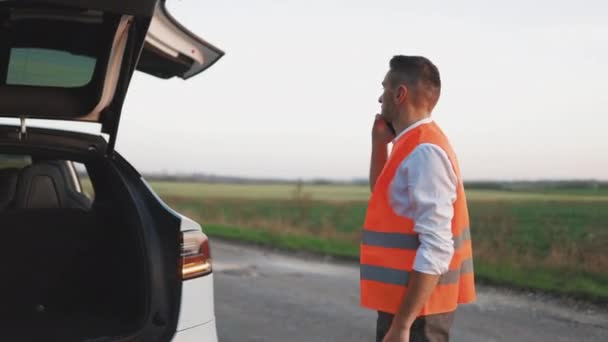 Electric car accident on the road. Man with reflective vest calling by phone about breakdown in her electric car assistance services, help repair. Emergency stop sign. — Stock Video
