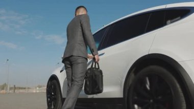 Genç yakışıklı işadamı elektrikli arabaya yürüyor. Kapıyı açar ve içeri girer. İnsanlar ve ulaşım. Başarı. Zenginlik