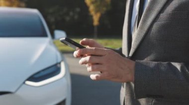 İşadamı mobil uygulama kullanarak otomatik çalışan bir elektrikli arabayı kontrol ediyor. Otonom otomatik pilot sürücüsüz araba. Akıllı telefon uygulaması. Algılayıcı tarama yolu ileride araçlar için, tehlike, hız limitleri.