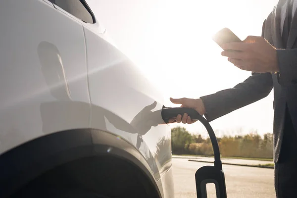 El hombre de negocios está conectando el cable de alimentación a un coche eléctrico. Recarga de coches eléctricos de lujo. Vehículo eléctrico de carga masculino ambientalmente consciente. Hombre enchufando coche eléctrico — Foto de Stock