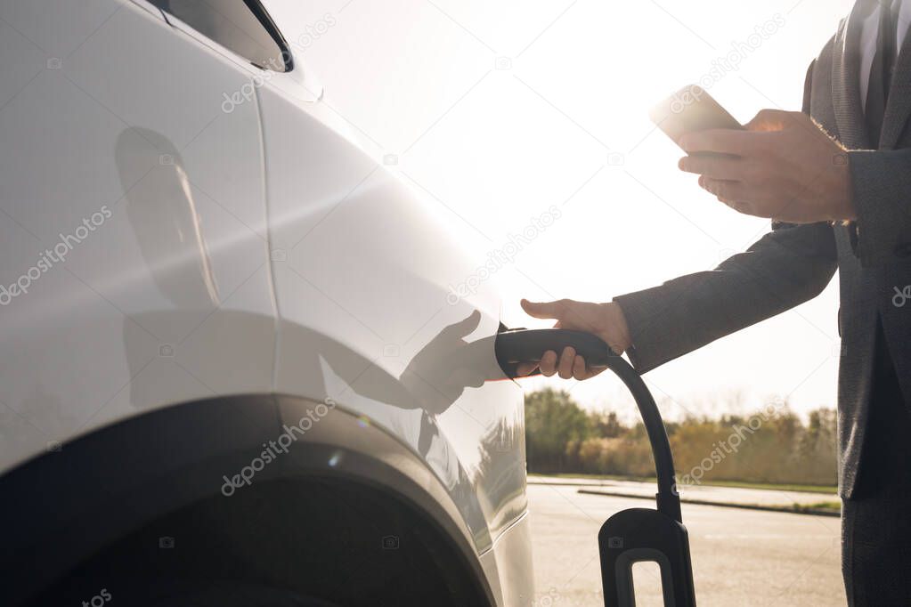 Senior businessman is plugging in power cord to an electric car. Luxury electrical car recharging. Environmentally conscious male charging electric vehicle. Man plugging in electric car