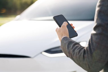 İşadamı mobil uygulama kullanarak otomatik çalışan bir elektrikli arabayı kontrol ediyor. Otonom otomatik pilot sürücüsüz araba. Akıllı telefon uygulaması. Algılayıcı tarama yolu ileride araçlar için, tehlike, hız limitleri.