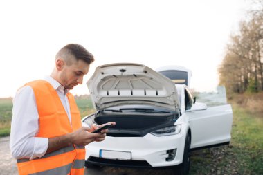 Kırsal yolda kalan genç üzgün işadamının portresi, akıllı telefonu kullanarak tahliyeciyi boşaltmaya yardım ediyor. Bir adam akıllı telefonunu kullanıyor çünkü elektrikli arabası bozuk..