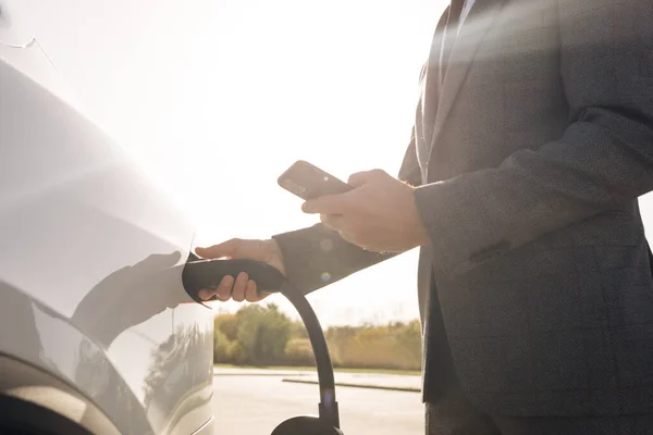 Empresario desenchufando coche eléctrico de la estación de carga. Lujo coche eléctrico blanco completo. Desconectar el cable cuando el llenado de energía eléctrica compite. — Foto de Stock