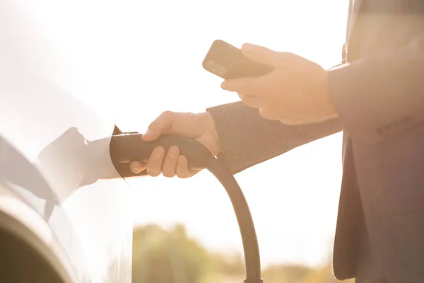 Oigenkännlig affärsman kopplar ur elbilen. Lyxig vit elbil full. Elfyllning konkurrerar och kabeln kopplas bort. Spara ekologi alternativ energi hållbar för framtiden — Stockfoto