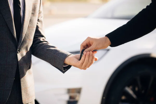 Manlig hand ger en bilnycklar till manlig hand i bilen återförsäljare närbild. Okänd bilförsäljare och en man som köpte ett fordon. Återförsäljare ger nyckel till ny ägare i auto show eller salong — Stockfoto