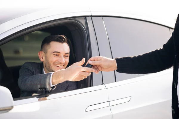 Młody szczęśliwy mężczyzna odbierający kluczyki do jej nowego samochodu. Dealer daje klucz do nowego właściciela w auto show lub salonie. Sprzedawca samochodów wykończenie czynienia samochodu — Zdjęcie stockowe
