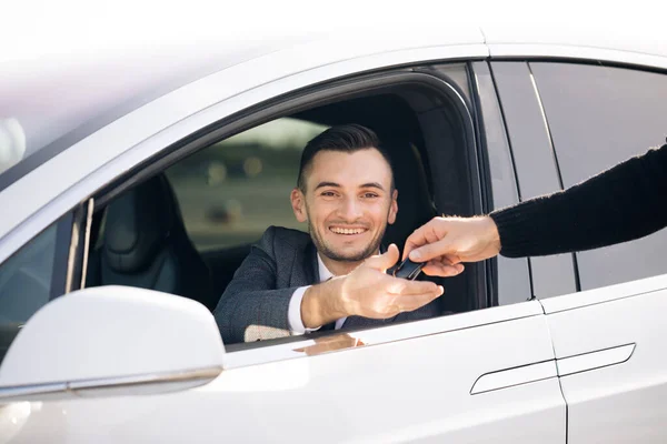 Ung lycklig man mottar bilnycklarna till hennes nya bil. Återförsäljare ger nyckel till ny ägare i auto show eller salong — Stockfoto